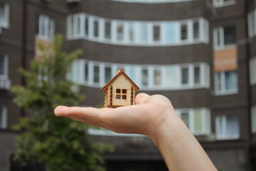 Wooden house in hand against the background of an apartment building