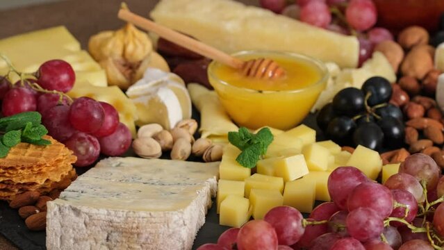 Cheese plate with camembert brie parmesan maasdam dutch cheese. Assortment of spanish or italian antipasti snack with cheese, nuts, bread, grapes, dates, figs. Top view flat lay background slow motion