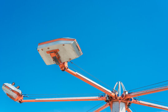Rotating cars and sweeps around center shaft of hurricane ride with cylinder piston under sunny blue sky in Dallas, Texas, America