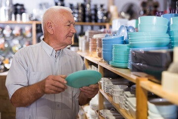 Portrait of focused mature man buyer choosing dishes at decor store