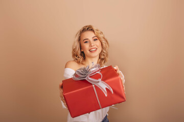 Happy young woman smiling in white blouse gives Christmas gift box isolated beige background. Copy Space. Christmas concept. 