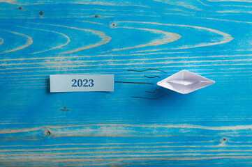 Origami made paper boat pulling a 2023 sign cut into a wooden plate