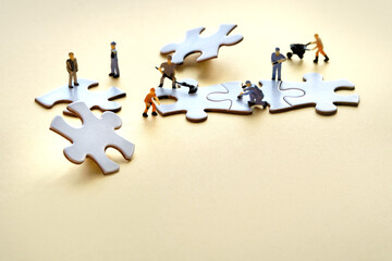 Team of tiny worker miniature figures on linked jigsaw puzzle pieces on golden yellow paper, space. Closeup on white jigsaw puzzle elements. Creative Team work in construction, development, logistics.