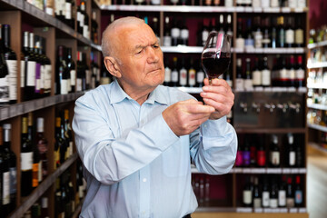 Portrait of positive man tasting red wine at wine shop