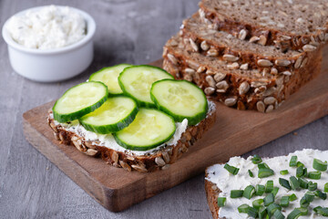 Slices of rye bread with cottage cheese and cucumbers on grey background