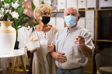 Portrait of senior married couple in protective mask with purchases in hands in store