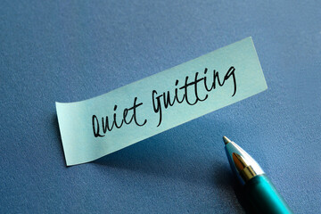 Text words Quiet Quitting on mint green post it note with pen on blue paper. Close-up on sticky...