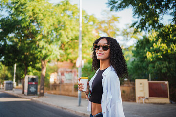 Young woman having a coffee and having a walk in the city. She is looking at camera.