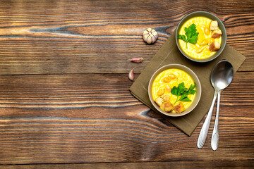 Vegetarian autumn pumpkin traditional soup with seeds, creamy silky texture, cilantro parsley dill greens, croutons, bread, garlic on wooden background. healthy vegan food concept, Top view