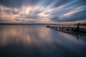 Fototapeta na wymiar Long exposure reflection of a pier, beautiful colorful clouds and iron pier at sunset time long exposure shot and movement feeling concept