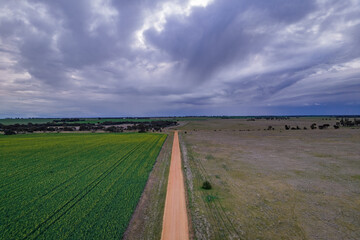 Looking down on a dirt road in a country setting with storm clouds on the horizon.