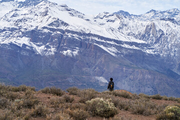 Fototapeta na wymiar young man standing contemplating a snow capped mountain in the middle of the Andes Mountains of Chile