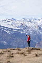 young red haired woman with red jacket and backpack, taking pictures with her phone in the middle of the Andes mountain range in Chile