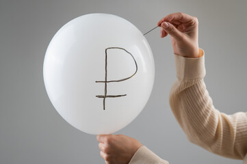 Caucasian woman pops a balloon with a ruble inscription with a needle. 