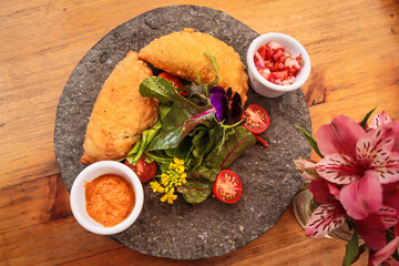 Latin American fried empanadas with sauce and salad decorated with flowers.  Peruvian food.  Cheese and ham empanadas.  Top view of the plate and a vase with flowers.