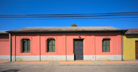 Facade of a one-floor traditional adobe house in a small south american town under blue sky (Talca, Maule, Chile) 