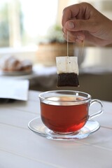 Woman taking tea bag out of cup at white wooden table indoors, closeup