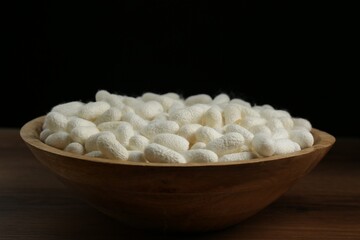 White silk cocoons in bowl on wooden table, closeup