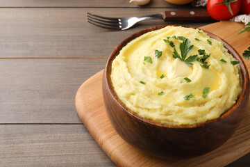 Bowl of freshly cooked mashed potatoes with parsley served on wooden table, closeup. Space for text