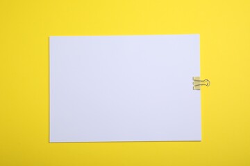 Sheet of paper with clip on yellow background, top view