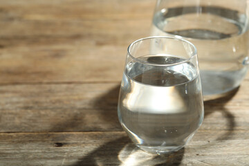 Glass of water on wooden table, space for text. Refreshing drink