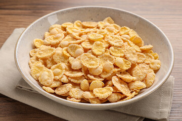Bowl of tasty corn flakes on wooden table, closeup