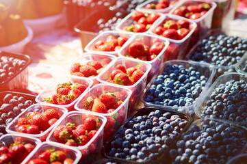 Strawberries and blueberries on a farmer's market stall on a sunny day. Fresh berries are laid out in even rows. Healthy food concept