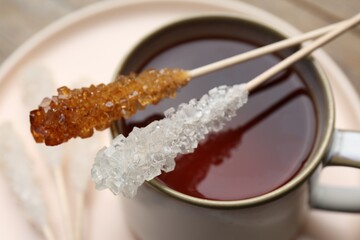 Sticks with sugar crystals and cup of tea on table, closeup