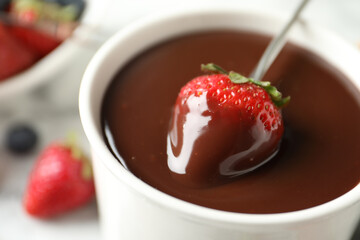 Dipping strawberry into fondue pot with chocolate, closeup