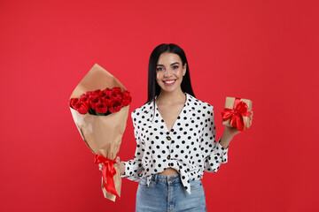Happy woman with tulip bouquet and gift box on red background. 8th of March celebration