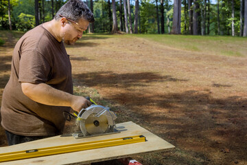 Using circular saw in hand, worker cuts plywood with the help of a circular saw held his hands