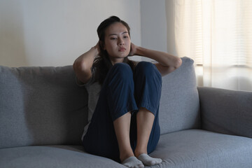 Asian woman covering her face feeling lonely and depressed sit on sofa in the room