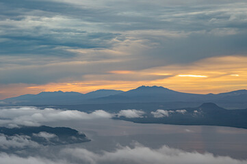 曇り空の朝の山のシルエットと湖の上に漂う雲。北海道の津別峠で。