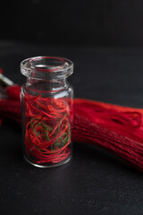 hilos color rojo dentro de botella de vidrio con fondo negro y madejas 