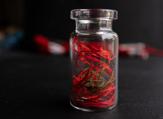 hilos color rojo dentro de botella de vidrio con fondo negro y madejas 