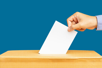 Hand voter holding ballot paper putting into the voting box at place election against a blue background