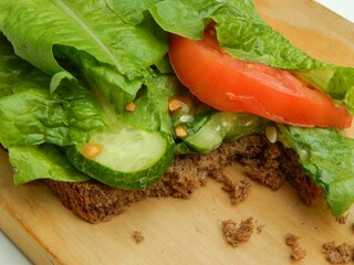Vegetarian sandwich lying on a wooden board, selenium salad, cucumbers, tomatoes on a piece of rye bread