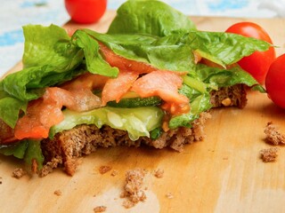 Vegetarian sandwich lying on a wooden board, selenium salad, cucumbers, tomatoes on a piece of rye bread