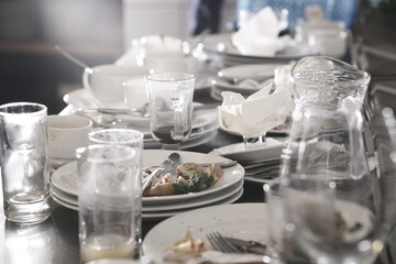 Dirty plates and glasses after a meal in the kitchen in the restaurant. Heap or pile of unclean glass and plates of breakfast or lunch table.