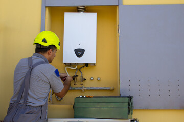 Plumber on a ladder with a wrench while repairing and servicing a gas boiler in anticipation of...