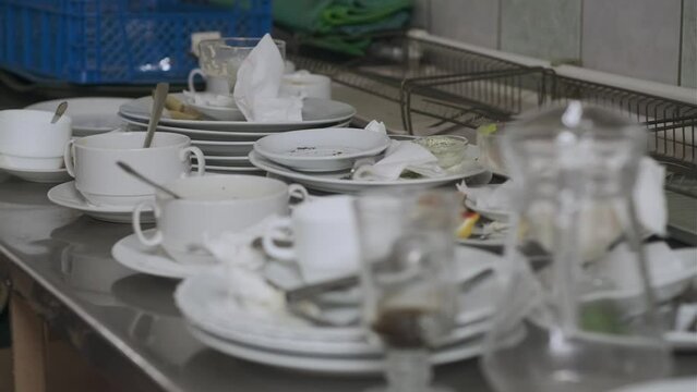 Dirty plates and glasses after a meal in the kitchen in the restaurant. Heap or pile of unclean glass and plates of breakfast or lunch table.