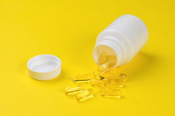 Fish oil capsules spilling out of a white bottle on a yellow background.