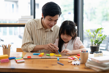 Obraz premium Young asian father and daughter plasticine or play dough on a table dough together