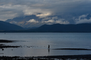 A man wades along the shore of Resurrection Bay near Seward, Alaska, at dusk.