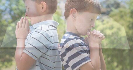 Naklejka premium Multiple exposure of caucasian elementary boys praying against trees and bible on table