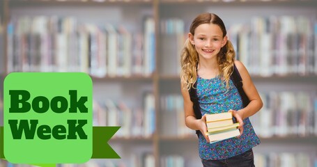 Book week text over portrait of smiling caucasian elementary girl standing with books in library