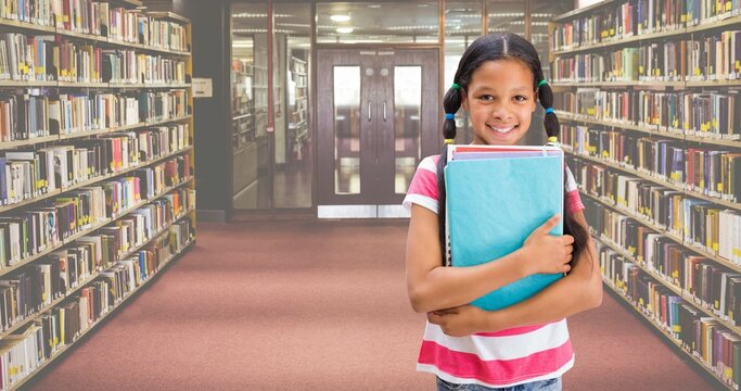 Portrait of smiling biracial elementary girl holding books while standing in library - Powered by Adobe