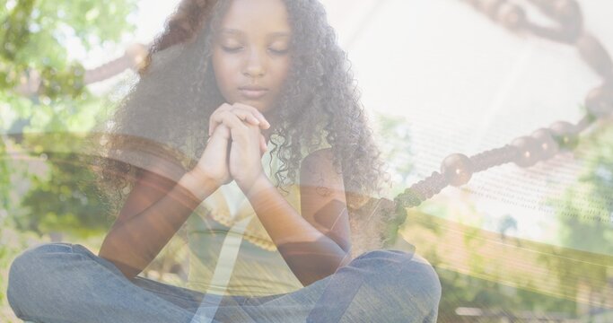 Multiple exposure of biracial elementary girl praying against trees and rosary on bible