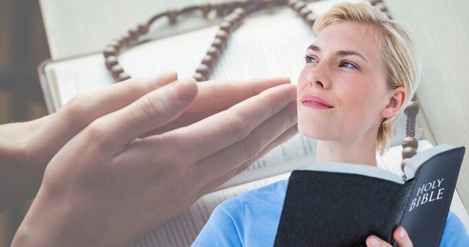 Caucasian young woman holding bible while looking away with hands clasped on book in background