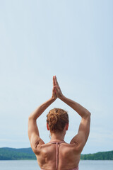 close-up back view mature woman in pink sportswear practices yoga on a wooden deck near the sea.